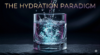A cinematic macro shot of pure, crystal-clear water pouring into a sleek geometric glass. The water glows from within with tiny, luminescent cyan and magenta hydrogen bubbles. The background is a luxurious dark slate void. Integrated title: THE HYDRATION PARADIGM.